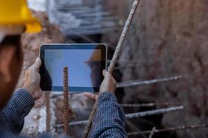 architect or civil engineer with hardhat on construction site checking schedule on tablet computer photo