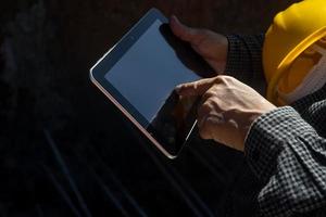 architect or civil engineer with hardhat on construction site checking schedule on tablet computer photo