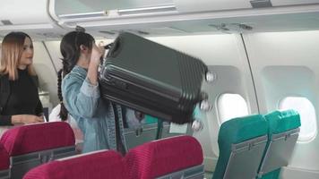 une passagère asiatique en file d'attente a mis ses bagages dans le stockage de l'avion. concept de voyage en avion video