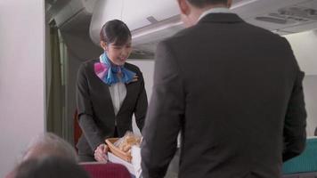 Asian cabin crew or flight attendant pushing cart to serving foods and drinks to passengers at seat on the airplane cabin. airline service career video