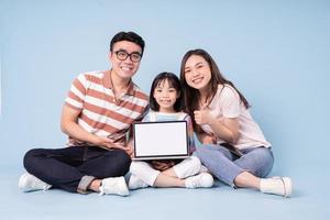 imagen de una joven familia asiática usando una laptop con fondo azul foto