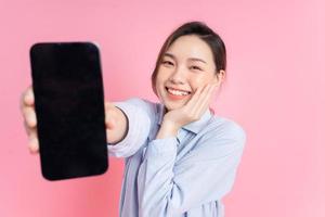 Image of young Asian girl holding smartphone on pink background photo