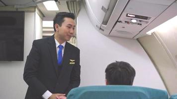 Asian smiling male cabin crew or steward talking to passenger ask for service on airplane cabin. business airline travel. video