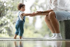 lindo concepto de familia de niño pequeño, bebé aprendiendo a caminar con el padre y la madre para ayudar a cuidar y tomar la mano, primer paso con el apoyo de los padres de la infancia, pequeño retrato de amor niño pequeño en casa foto