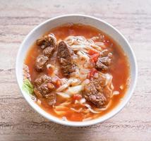 Beef noodle ramen meal with tomato sauce broth in bowl on bright wooden table, famous chinese style food in Taiwan, close up, top view, copy space photo