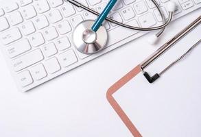 Stethoscope on keyboard on white table background. Online medical information treatment technology office concept, top view, flat lay, copy space photo