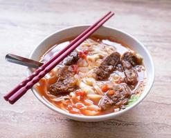 Beef noodle ramen meal with tomato sauce broth in bowl on bright wooden table, famous chinese style food in Taiwan, close up, top view, copy space photo