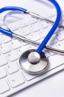 Blue stethoscope on computer keyboard on white table background. Online medical information treatment technology concept, close up, macro, copy space photo