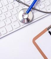 Stethoscope on computer keyboard on white background. Physician write medical case long term care treatment concept, top view, flat lay, copy space photo