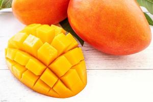 Beautiful chopped mango with green leaves on bright white color timber background. Above Top view, flat lay, copy space, close up. Tropical fruit concept. photo