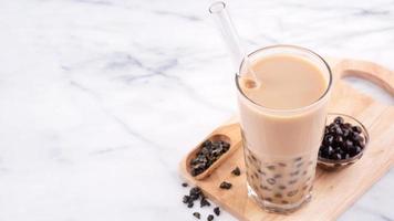 té de leche con burbujas de bolas de perla de tapioca, bebida popular de taiwán, en vaso con paja sobre mesa blanca de mármol y bandeja de madera, primer plano, espacio para copiar. foto