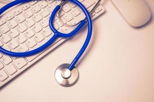 estetoscopio azul en el teclado de la computadora en el fondo de la mesa blanca. concepto de tecnología de tratamiento de información médica en línea, primer plano, macro, espacio de copia foto