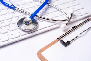 Stethoscope on computer keyboard on white background. Physician write medical case long term care treatment concept, close up, macro, copy space photo