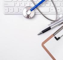 Stethoscope on computer keyboard on white background. Physician write medical case long term care treatment concept, top view, flat lay, copy space photo