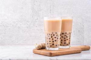 Popular Taiwan drink - Bubble milk tea with tapioca pearl ball in drinking glass on marble white table wooden tray background, close up, copy space photo