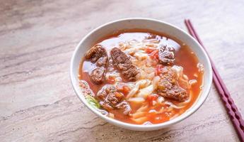 Beef noodle ramen meal with tomato sauce broth in bowl on bright wooden table, famous chinese style food in Taiwan, close up, top view, copy space photo