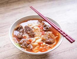 Beef noodle ramen meal with tomato sauce broth in bowl on bright wooden table, famous chinese style food in Taiwan, close up, top view, copy space photo