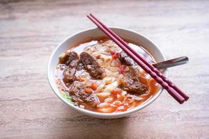 Beef noodle ramen meal with tomato sauce broth in bowl on bright wooden table, famous chinese style food in Taiwan, close up, top view, copy space photo