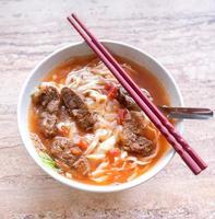 Beef noodle ramen meal with tomato sauce broth in bowl on bright wooden table, famous chinese style food in Taiwan, close up, top view, copy space photo