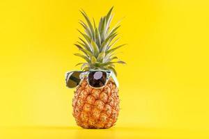 Creative pineapples with sunglasses isolated on yellow background, summer vacation beach idea design pattern, copy space, close up, blank for text photo