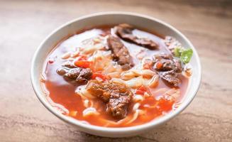 Beef noodle ramen meal with tomato sauce broth in bowl on bright wooden table, famous chinese style food in Taiwan, close up, top view, copy space photo