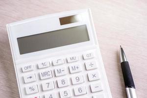 White calculator and pen on bright wooden table, analytics and statistics of financial profit, investment risk concept, copy space, top view flat lay photo