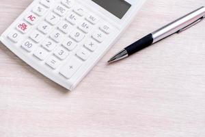 White calculator and pen on bright wooden table, analytics and statistics of financial profit, investment risk concept, copy space, top view flat lay photo