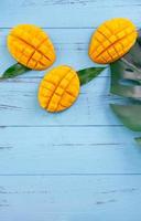 Fresh mango - beautiful chopped fruit with green leaves on bright blue timber background. Tropical fruit design concept. Flat lay. Top view. Copy space photo