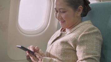 Asian female passenger sitting at seat using mobile phone and watching out of airplane window. airline travel for vacation video