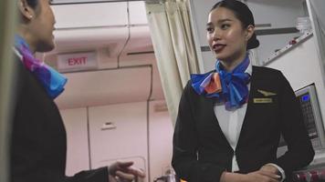 twee Aziatische vrouwelijke stewardess praten samen in de kombuis terwijl ze een pauze nemen in het vliegtuig. vrolijke stewardessen bij de voedselbereidingsruimte video