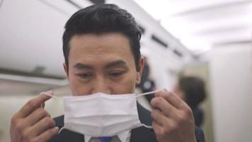 Portrait of Asian male steward wearing medical face mask to prevent Coronavirus on airplane cabin. Airline business responsibility service and support travel during virus epidemic video