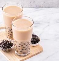 bebida popular de taiwán - té de leche de burbujas con bola de perla de tapioca en vaso de bebida sobre fondo de bandeja de madera de mesa blanca de mármol, primer plano, espacio de copia foto