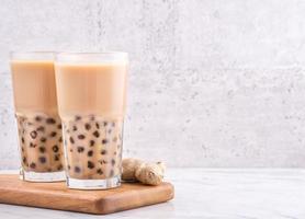 Popular Taiwan drink - Bubble milk tea with tapioca pearl ball in drinking glass on marble white table wooden tray background, close up, copy space photo