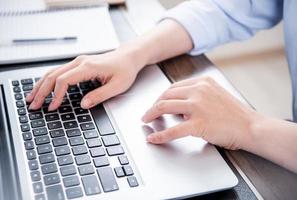 Business concept. Woman in blue shirt typing on computer with coffee on office table, backlighting, sun glare effect, close up, side view, copy space photo