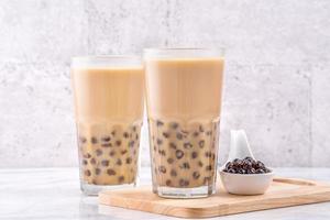 Popular Taiwan drink - Bubble milk tea with tapioca pearl ball in drinking glass on marble white table wooden tray background, close up, copy space photo