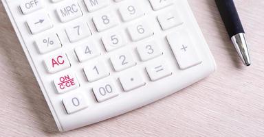 White calculator and pen on bright wooden table, analytics and statistics of financial profit, investment risk concept, copy space, macro, close up photo