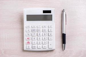 calculadora blanca y bolígrafo sobre mesa de madera brillante, análisis y estadísticas de beneficios financieros, concepto de riesgo de inversión, espacio de copia, vista superior plana