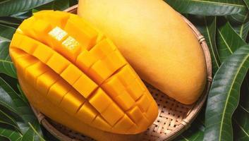 Fresh Mango - Juicy diced fruit in bamboo sieve on green color leaves background. Tropical summer concept. Top view, close up, macro, copy space. photo