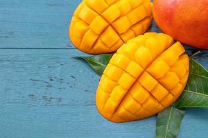 Fresh mango - beautiful chopped fruit with green leaves on dark blue timber background. Tropical fruit design concept. Flat lay. Top view. Copy space photo