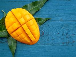 Fresh mango - beautiful chopped fruit with green leaves on dark blue timber background. Tropical fruit design concept. Flat lay. Top view. Copy space photo