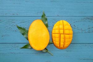 Fresh mango - beautiful chopped fruit with green leaves on dark blue timber background. Tropical fruit design concept. Flat lay. Top view. Copy space photo