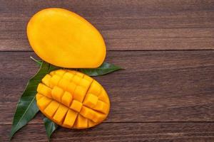 Fresh mango - beautiful chopped fruit with green leaves on dark wood background. Tropical fruit design concept. Flat lay. Top view. Copy space. photo