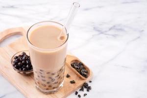 té de leche con burbujas de bolas de perla de tapioca, bebida popular de taiwán, en vaso con paja sobre mesa blanca de mármol y bandeja de madera, primer plano, espacio para copiar. foto