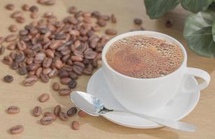 taza de café con leche y granos de café sobre una mesa de madera con plantas y fondo de pared de ladrillo blanco. foto