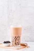 Popular Taiwan drink - Bubble milk tea with tapioca pearl ball in drinking glass on marble white table wooden tray background, close up, copy space photo