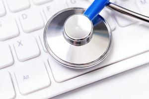 Blue stethoscope on computer keyboard on white table background. Online medical information treatment technology concept, close up, macro, copy space photo