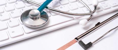 Blue stethoscope on computer keyboard on white table background. Online medical information treatment technology concept, close up, macro, copy space photo