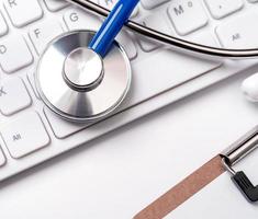 Stethoscope on computer keyboard on white background. Physician write medical case long term care treatment concept, close up, macro, copy space photo