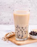 Popular Taiwan drink - Bubble milk tea with tapioca pearl ball in drinking glass on marble white table wooden tray background, close up, copy space photo