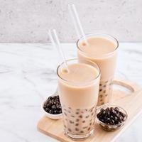 Tapioca pearl ball bubble milk tea, popular Taiwan drink, in drinking glass with straw on marble white table and wooden tray, close up, copy space. photo